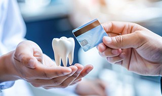 Fake tooth levitating over dentist’s hands as patient hands over a light blue credit card