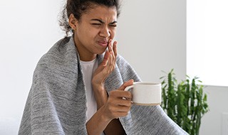 Woman experiencing toothache while drinking tea at home