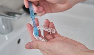 Patient using toothbrush to clean aligner