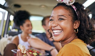 Woman smiling while eating meal in car with friends