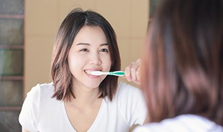 Woman in white shirt brushing teeth in mirror