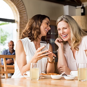 Smiling friends looking at phone in coffee shop