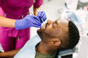 Man with brown hair undergoing exam by dentist with magenta scrubs and blue gloves