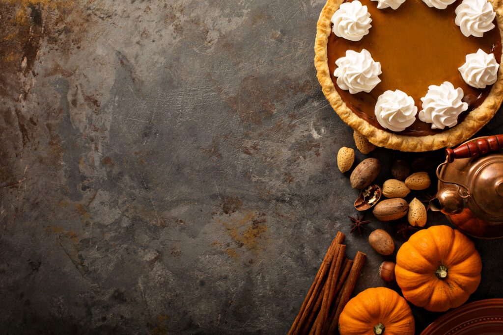 Pumpkin pie with pecans, cinnamon, and tea kettle on scratched gray surface